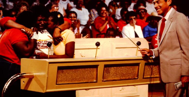 Contestants hugging on game show set with host looking on