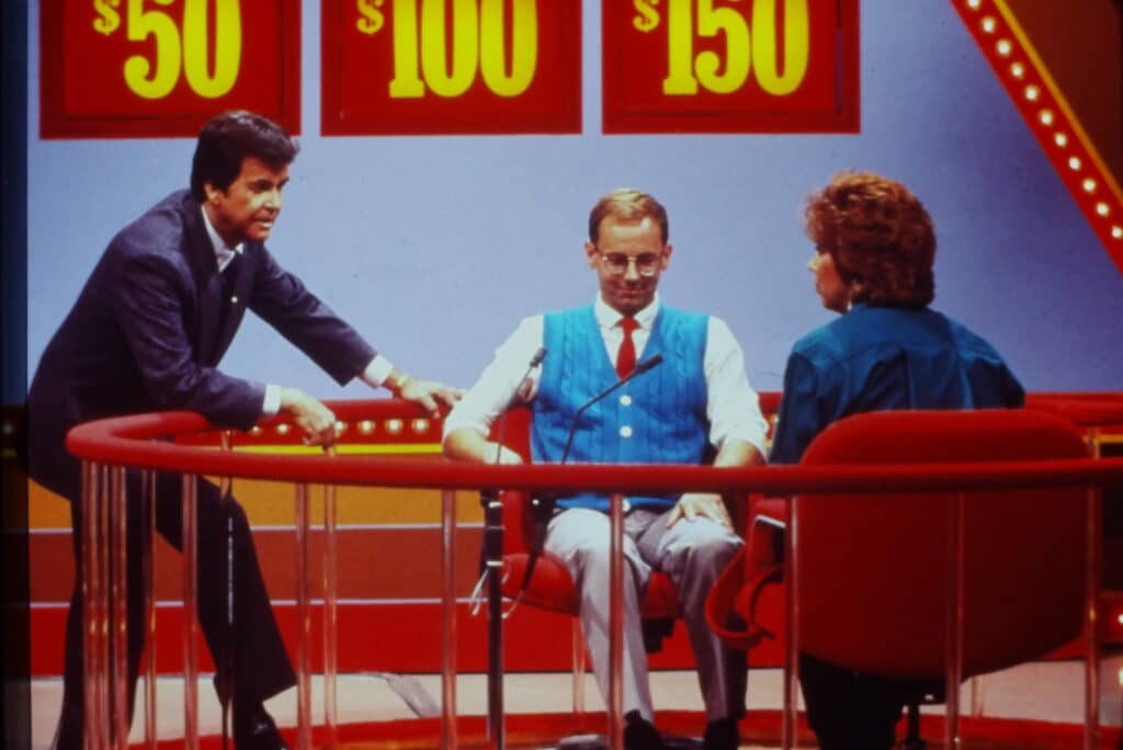 Two contestants on set of Pyramid while host looks on