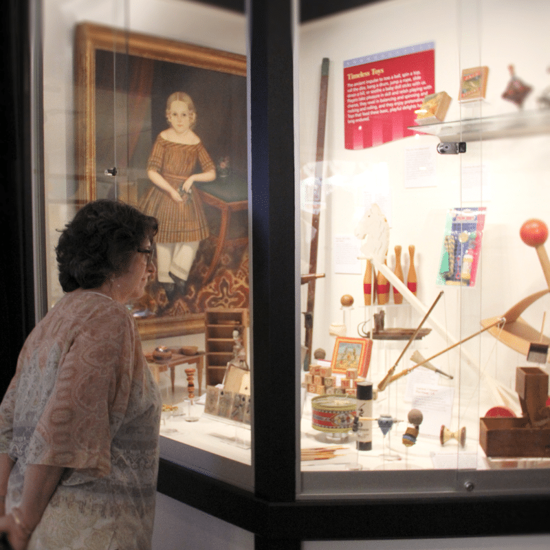 Woman viewing an artifact case in America at Play.